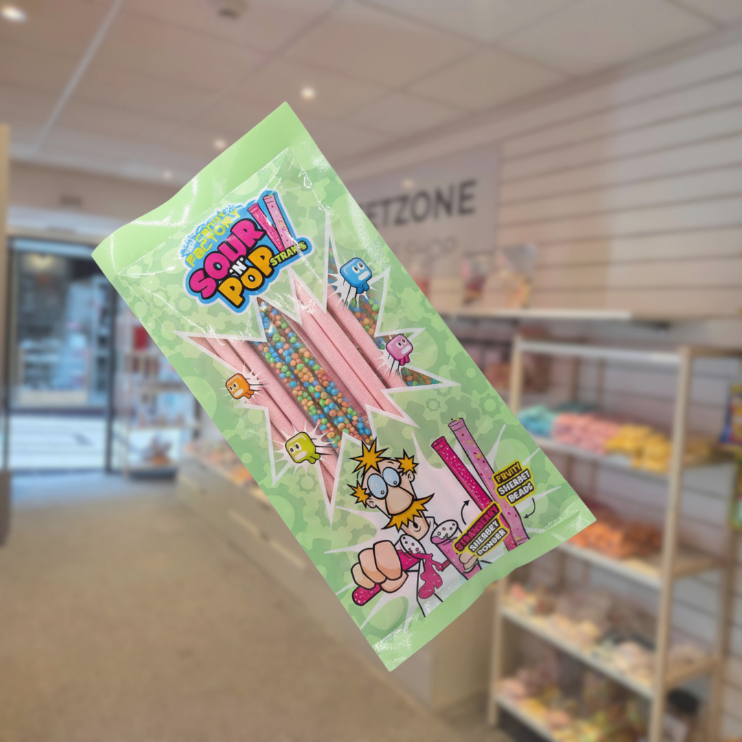 Crazy Candy Factory Sour n Pop Straws in a green packet with pink straws visible through the window, against a sweet-shop background.