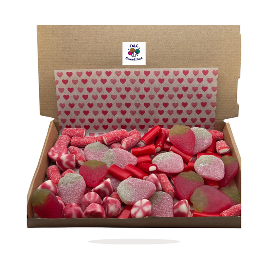An open brown cardboard gift box filled with assorted red and pink candies, gummy strawberries, and sugar-coated sweets, with a heart-patterned tissue liner inside and a visible D&G Peppermint logo sticker on the inner lid.